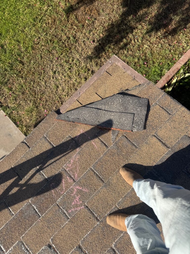 Roofer inspecting an asphalt shingle roof with a missing shingle and chalk-marked wind damage