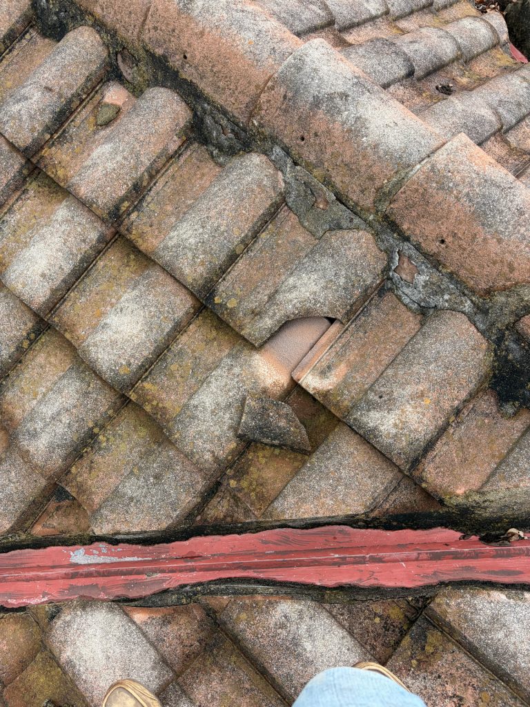 Weathered clay tile roof with moss, a cracked tile and exposed red flashing